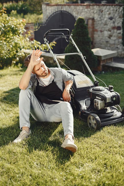 A man with a neatly groomed beard and styled hair is wearing a light grey shirt with rolled-up sleeves and light grey trousers while operating a modern, electric grass trimmer to edge a well-maintaine